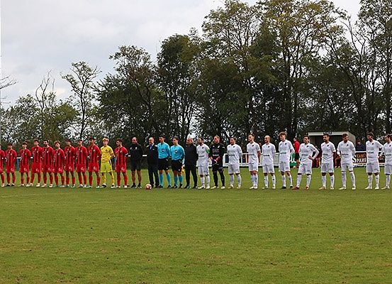 Zwei Fußballmannschaften in roten und weißen Trikots stehen auf einem Rasenfeld und warten wahrscheinlich darauf, ein Spiel zu beginnen.