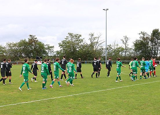 Fußballspieler in grünen und schwarzen Uniformen sind auf dem Feld, wahrscheinlich den Beginn eines Spiels. Das Feld hat weiße Linien. Bäume säumen den Rand des Feldes.