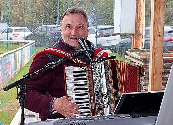 Ein Mann spielt Akkordeon bei einem Konzert, steht vor einem Mikrofon, mit geparkten Autos dahinter.