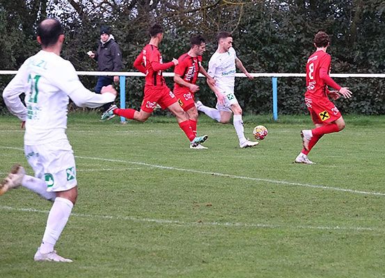Fußballspieler in roten und weißen Trikots spielen auf einem Feld. Ein Spieler in Rot ist dabei, den Ball zu schießen.