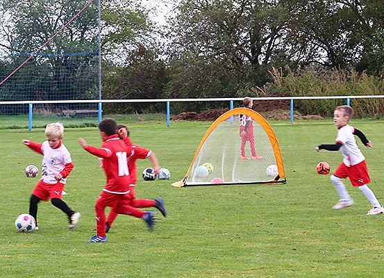 Eine Gruppe junger Jungen in roten und weißen Uniformen spielt Fußball auf einem Feld mit einem Tornetz vor ihnen.