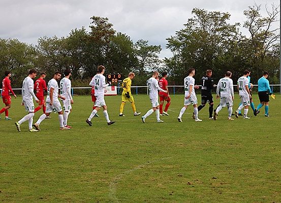 Fußballspieler in roten und weißen Trikots laufen auf dem Feld, möglicherweise am Ende eines Spiels. Ein Spielstand ist im Hintergrund zu sehen.
