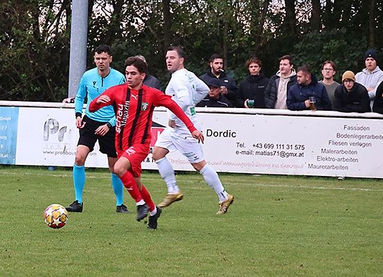 Fußballspieler in roten und weißen Trikots sind in einem Spiel engagiert. Ein Spieler versucht, den Ball zu schießen, während andere von den Seitenlinien zusehen.