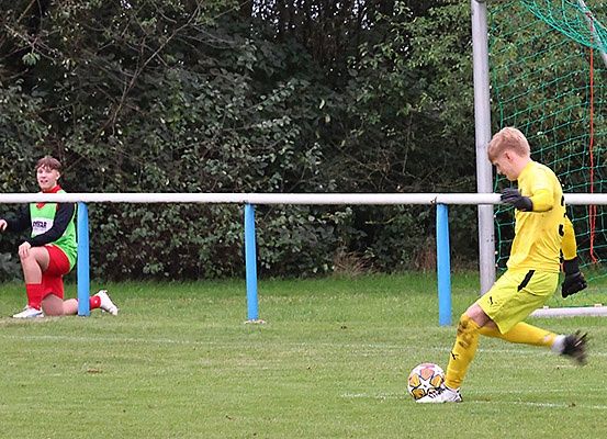 Zwei Fußballspieler auf einem Feld, einer in Gelb kickt einen Ball, der andere in Grün und Rot beobachtet.
