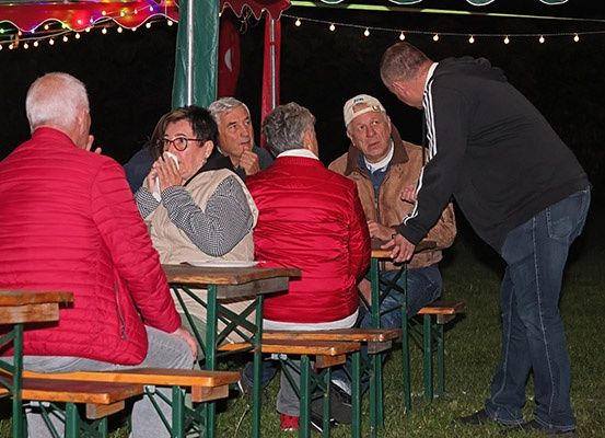 Eine Gruppe älterer Männer und Frauen sitzt an einem Tisch unter einem Zelt, vielleicht auf einem Festival.