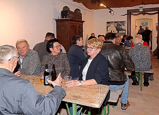 Mehrere ältere Menschen sitzen um einen Holztisch in einem Restaurant herum und trinken und essen. Flaschen Bier und Gläser stehen auf dem Tisch.