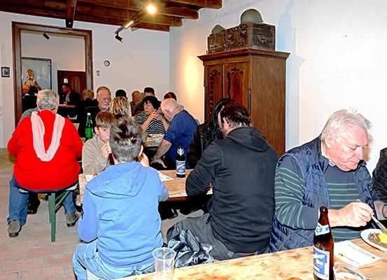 Eine Gruppe älterer Personen sitzt an einem Esstisch in einem rustikalen Restaurant und genießt ihre Mahlzeiten. Die Umgebung ist warm mit Holztischen und Stühlen, und Flaschen Bier sind vorhanden.