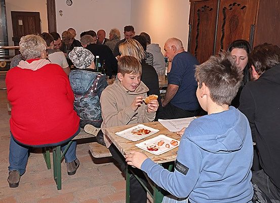 Eine Gruppe von Menschen sitzt an einem Tisch in einem Restaurant, isst und unterhält sich. Ein Junge isst ein Sandwich, während ein anderer Junge ihn beobachtet.
