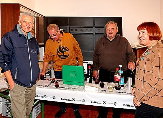 Vier Personen stehen um einen Tisch mit Flaschen, Gläsern und einer grünen Box. Sie scheinen bei einer Veranstaltung zu sein.