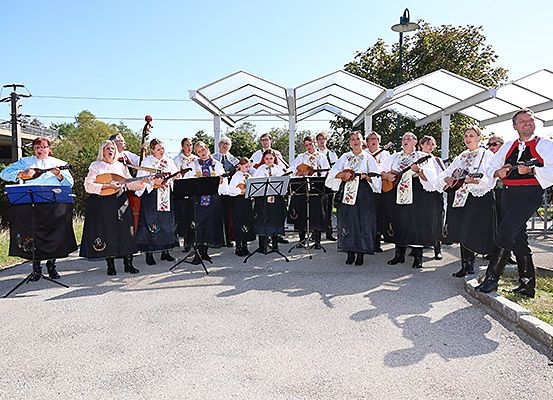 Eine Gruppe von Menschen in traditioneller Kleidung gibt ein Musikkonzert mit verschiedenen Instrumenten, darunter Lauten und Celli, unter einer weißen Struktur.