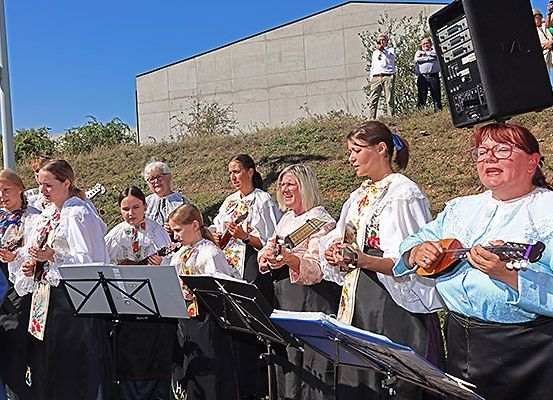 Eine Gruppe von Frauen in traditioneller Kleidung spielt Musikinstrumente auf einem Hügel, wobei ein Lautsprecher auf einer von ihnen sitzt, und Zuschauer im Hintergrund.