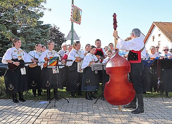 Eine Gruppe von Musikern in traditioneller Kleidung tritt an einem sonnigen Tag auf, wobei ein Mann im Vordergrund einen großen Bass spielt.