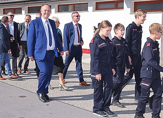 Mehrere Erwachsene und Kinder in Uniformen gehen auf einer Betonfläche vor einem Gebäude mit Fenstern.