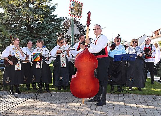 Eine Gruppe von Musikern in traditioneller Kleidung, die auf einer Straße mit einem roten Cello im Vordergrund auftreten.