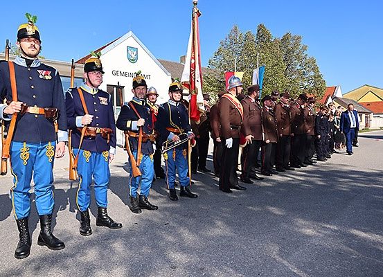 Soldaten in historischen Uniformen stehen in einer Reihe, Gewehre und Fahnen haltend, vor einem Gebäude.