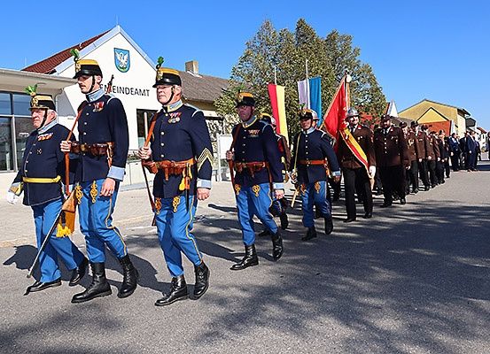 Ein Militärparade mit Soldaten in blauen Uniformen, die in einer Reihe mit Flaggen vor einem Gebäude marschieren.