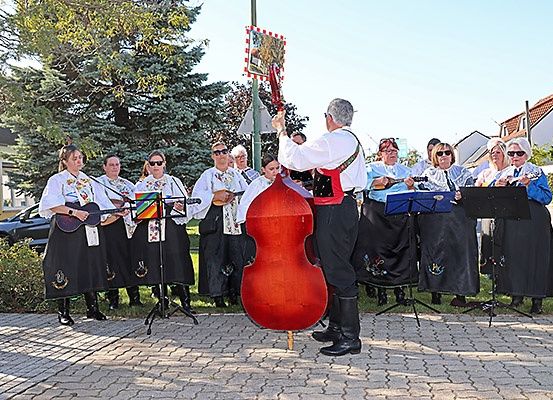 Eine Gruppe von Musikern steht in einer Reihe und hält Instrumente. Ein Mann vorne hält ein großes Cello. Sie tragen traditionelle Kleidung und Sonnenbrillen.