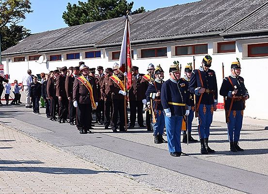 Eine Gruppe von Militärangehörigen steht in Formation vor einem Gebäude mit Zuschauern an der Seite.