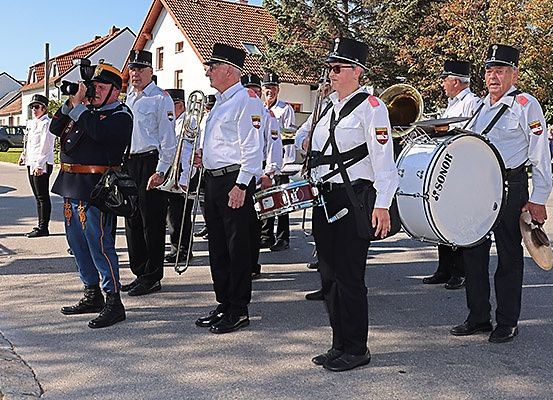 Eine Gruppe von Musikern in Uniform, die Musikinstrumente halten, tritt auf der Straße auf. Im Hintergrund sind einige Gebäude zu sehen.