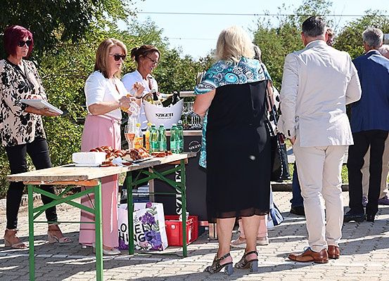 Eine Gruppe von Menschen versammelt sich um einen Tisch mit Essen und Getränken, zwei Frauen lächeln und unterhalten sich.