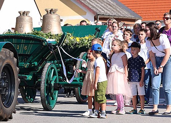 Ein grüner Oldtimer-Traktor mit Glocken wird an einem sonnigen Tag in einem Dorf von Kindern und Erwachsenen paradiert.