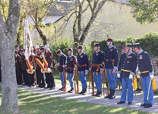 Eine militärische Parade von uniformierten Soldaten, die in einer Reihe auf einem gepflasterten Gehweg stehen, mit Zuschauern hinter ihnen.