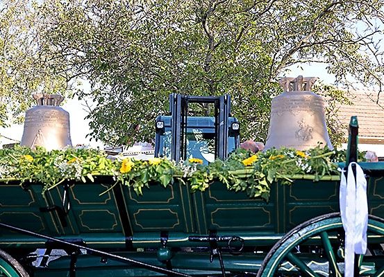 Ein grüner Wagen mit zwei Glocken, geschmückt mit Blumen und grünen Blättern. Dahinter ein Gabelstapler mit einer Person obenauf.