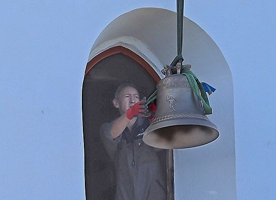 Eine Person mit roten Handschuhen hält eine Glocke mit einem grünen Band, das daran hängt, und scheint sie zu reparieren.