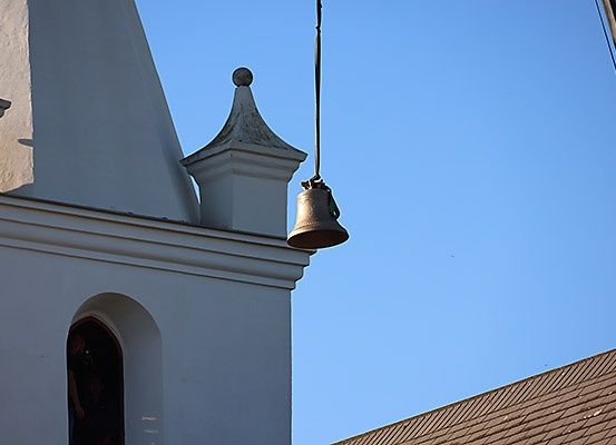 Eine Glocke hängt an einem Kirchturm bei klarem blauem Himmel, mit einer Person im Türeingang.