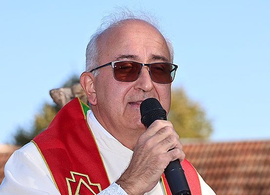 Ein älterer Mann in einer roten und weißen Robe und mit einer Sonnenbrille spricht in ein Mikrofon im Freien.