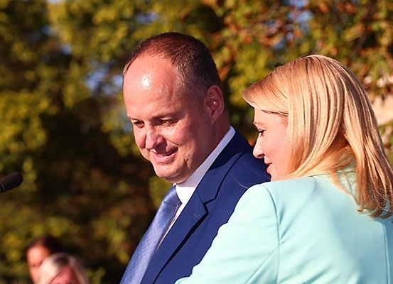 Ein Mann und eine Frau stehen eng nebeneinander mit einem Mikrofon davor und schauen sich an.
