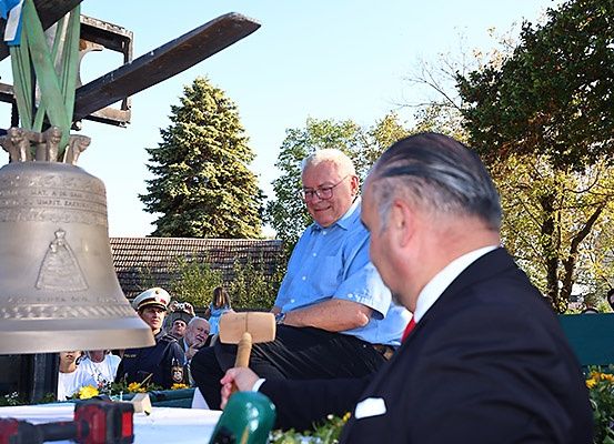 Ein Mann in einem Anzug schlägt mit einem Hammer auf eine Glocke, während ein anderer Mann in der Nähe sitzt, beide umgeben von Zuschauern.