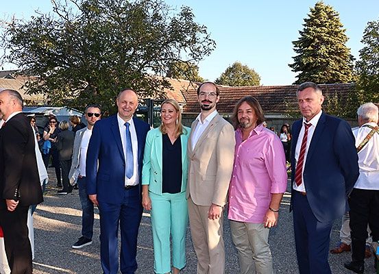 Eine Gruppe von Menschen steht draußen vor einem Gebäude. Eine Person trägt die Robe eines Priesters.