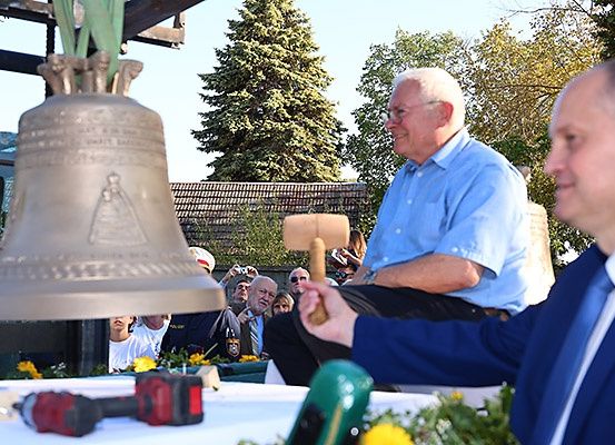 Ein Mann mit einem Hammer ist dabei, eine große Glocke zu läuten. Ein Mann im Anzug schaut zu.