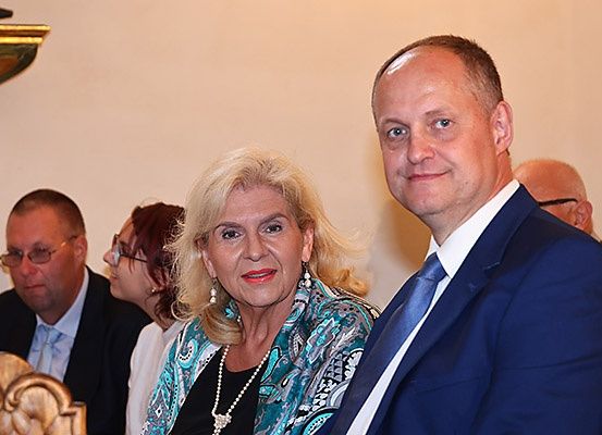 Eine Gruppe von Menschen in formeller Kleidung, darunter ein Mann und eine Frau, sitzen in einer Kirche, wahrscheinlich während einer Hochzeit.