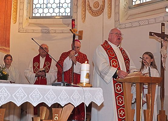 Eine religiöse Zeremonie in einer Kirche mit einem Priester, der aus einem Buch liest, Kerzen und Menschen, die vor einem Altar stehen.