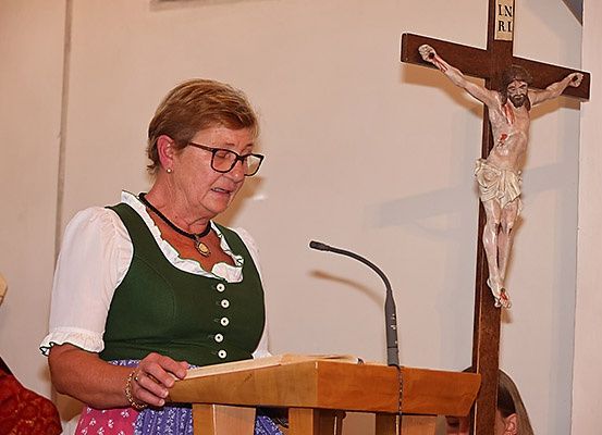 Eine Frau steht in einer Kirche an einem Podium und liest aus einem Buch. Hinter ihr ist ein Kruzifix an der Wand angebracht.