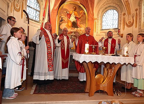 Priester und junge Leute stehen an einem Altar in einer Kirche. Ein Gemälde von Jesus Christus hängt hinter ihnen.
