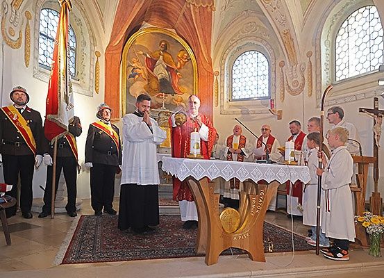 Priester führen eine Zeremonie in einer Kirche durch, mit einem Gemälde hinter dem Altar. Vorne stehen Menschen, darunter einige in Uniform, und andere stehen an den Seiten.