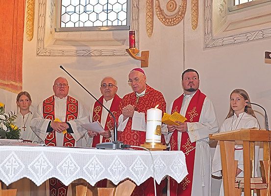 In einer Kirche findet eine religiöse Zeremonie mit einem Priester und vier Helfern, darunter zwei Frauen, statt, die Papiere und Kerzen halten.