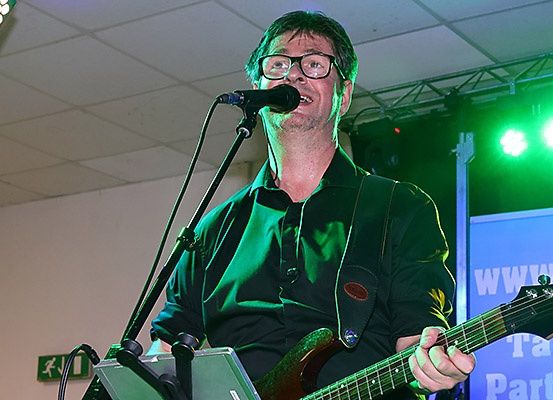 Ein Mann spielt eine E-Gitarre und singt in ein Mikrofon auf der Bühne mit grünen Lichtern.