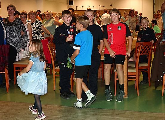 Eine Gruppe von Kindern und Erwachsenen in einem Saal, möglicherweise bei einer Zeremonie, mit einem Jungen, der eine Flasche Coca-Cola hält.
