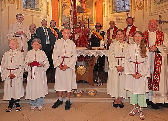 Eine Gruppe von Personen, einige in geistlicher Kleidung, steht in einer Kirche. Altar und Kerzen sind sichtbar, und alle scheinen für ein Foto zu posieren.