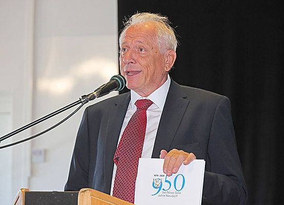 Ein Mann in Anzug und Krawatte spricht in ein Mikrofon am Rednerpult und hält ein Papier mit der Nummer 950.