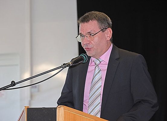 Ein Mann in einem Anzug steht an einem Rednerpult mit einem Mikrofon, wahrscheinlich hält er eine Rede oder Präsentation.