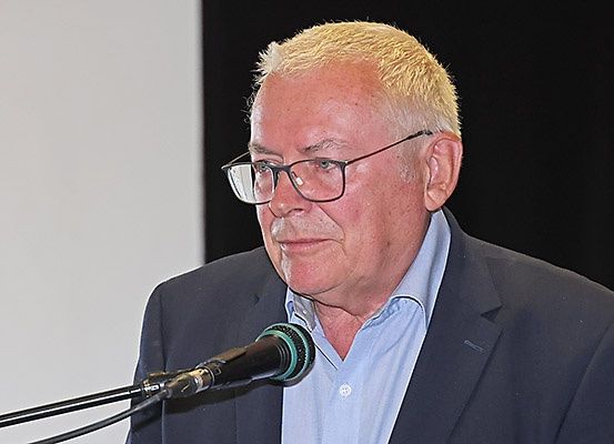 Ein älterer Mann in Anzug und Brille steht hinter einem Mikrofon und hält möglicherweise eine Rede.