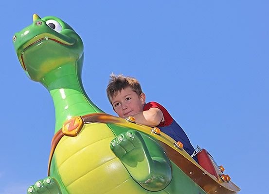 Ein junger Junge fährt auf einem sonnigen Tag eine riesige aufblasbare Dinosaurier-Attraktion.