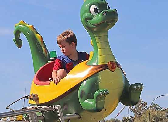 Ein junger Junge fährt auf einem grünen und gelben drachenförmigen Fahrgeschäft in einem Freiluft-Vergnügungspark.
