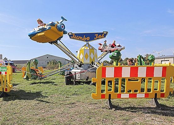 Eine bunte Karussellfahrt namens Jumbo Jet ist in Betrieb, mit Kindern, die den Ritt an einem sonnigen Tag genießen. Die Fahrt ist von Sicherheitsbarrieren umgeben.