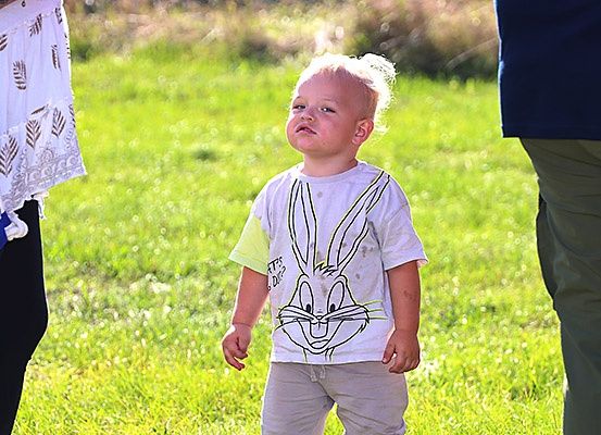 Ein kleiner Junge in einem Bugs Bunny-Shirt schaut zum Himmel, möglicherweise während er auf einem Rasenfeld spielt.